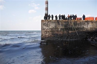 昨日，山東青島，清污人員正在海邊清理油污。