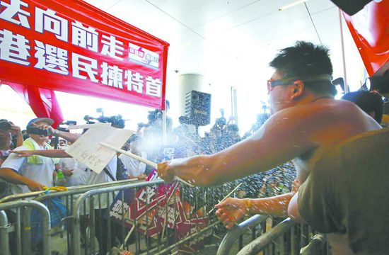 17日，在香港立法會(huì)外，一名反對政改的男子向支持派人群投擲標(biāo)牌。
